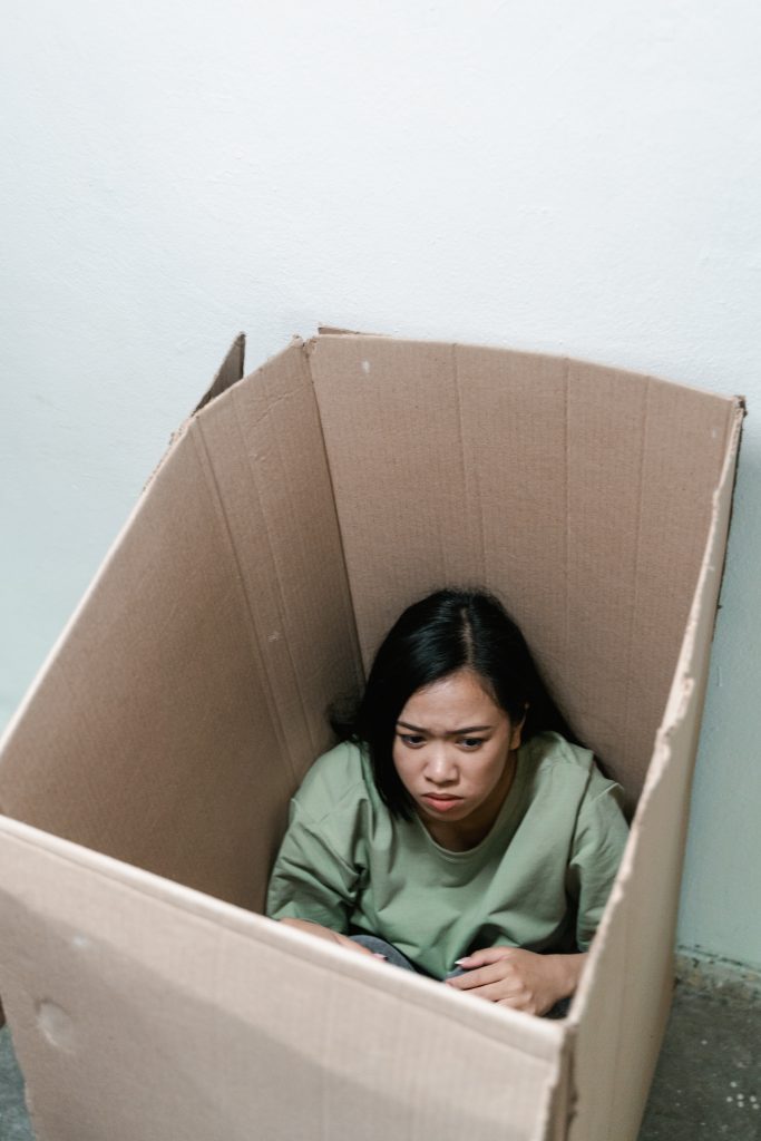 A woman with phobia, sitting inside a carton box, trying to hide from a feared object or situation.