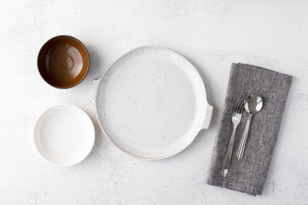 An aesthetic shot of an empty plate and bowls with neatly arranged cutlery on a white table, emphasizing the importance of intermittent fasting.