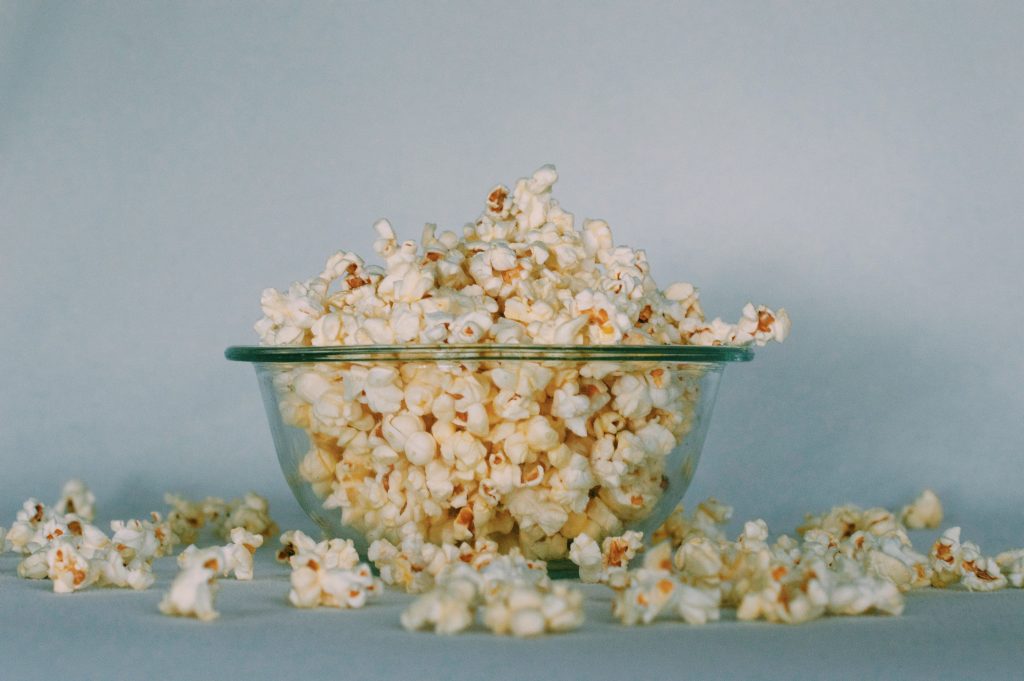 Popcorn, an excellent low-calorie, energizing snack, overflowing in a glass bowl with a few pieces spilled around.