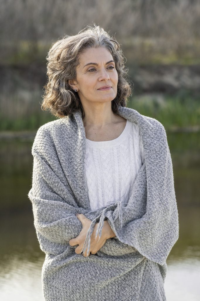 A candid shot of an elderly woman casually standing, highlighting that rheumatoid arthritis can develop at any age, with the risk increasing as people get older.