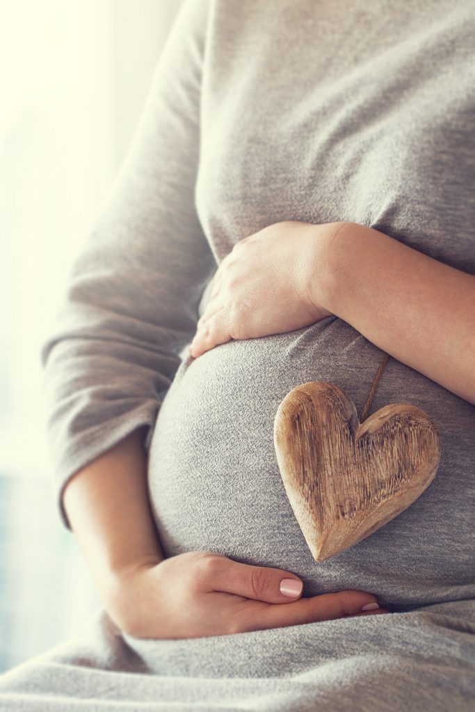 A pregnant woman holding a cute heart.