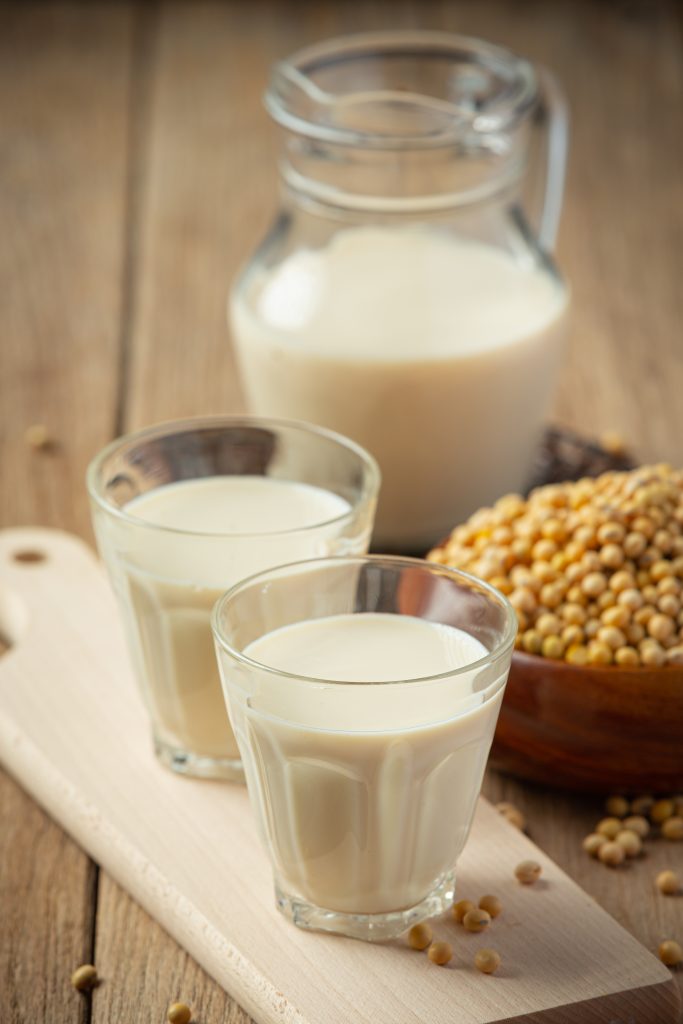 Two glasses of soymilk next to a jar filled with more soymilk and a bowl of soybeans, showcasing soymilk as a great alternative to cow's milk.