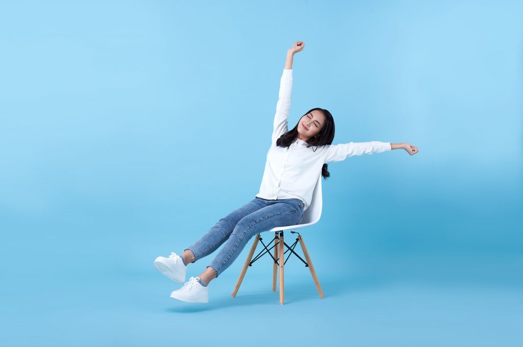 A woman sitting on a chair, performing a hand stretch exercise.