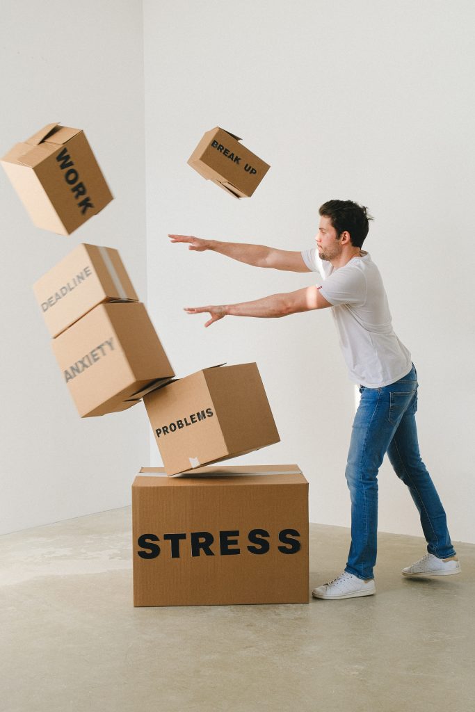 A man disrupting a stack of cartons labeled with words like "Problems," "Breakup," "Anxiety," "Deadline," "Work," and "Stress".
