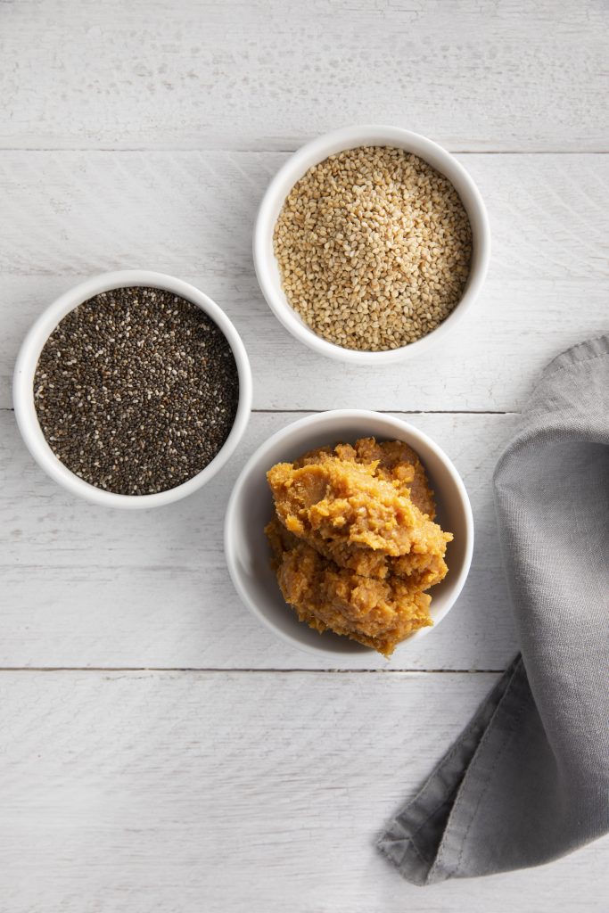 A top view shot of a variety of seeds, including sesame seeds, arranged in three bowls.