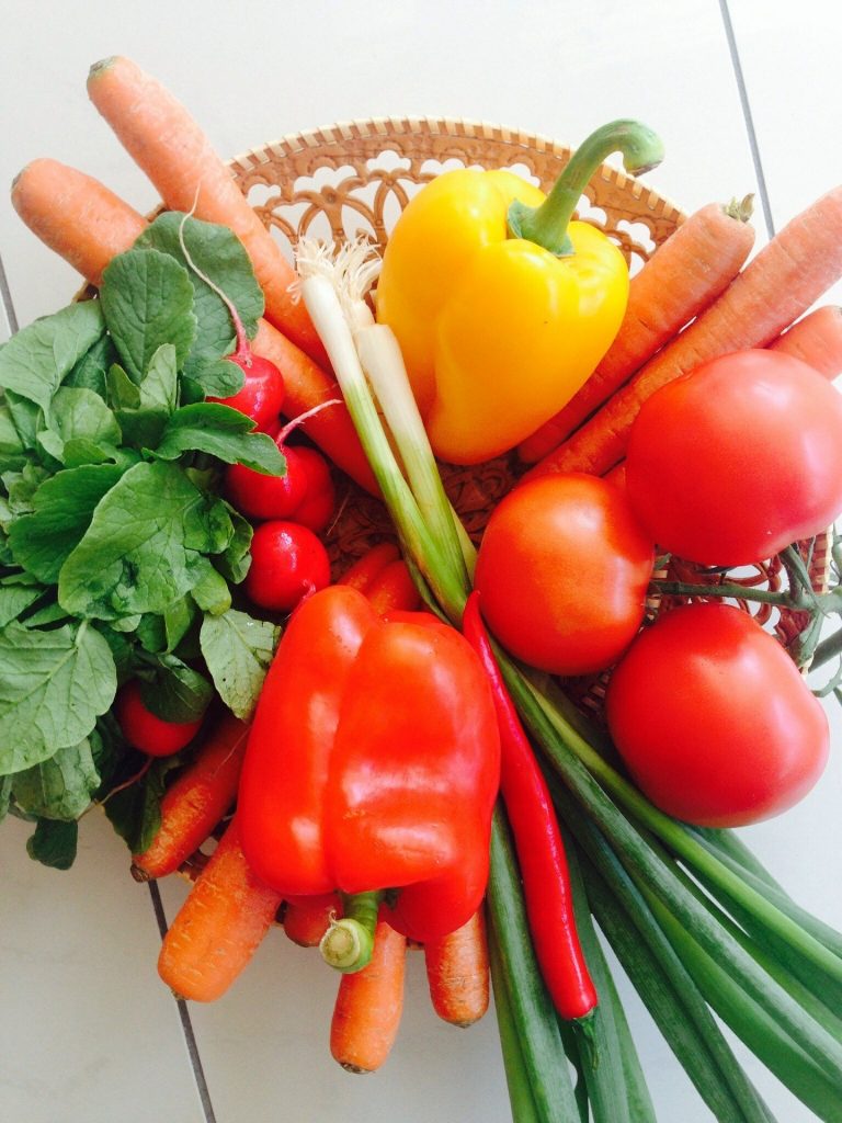 Colorful vegetables, including carrots, tomatoes, spinach, and green onions, arranged in a basket.