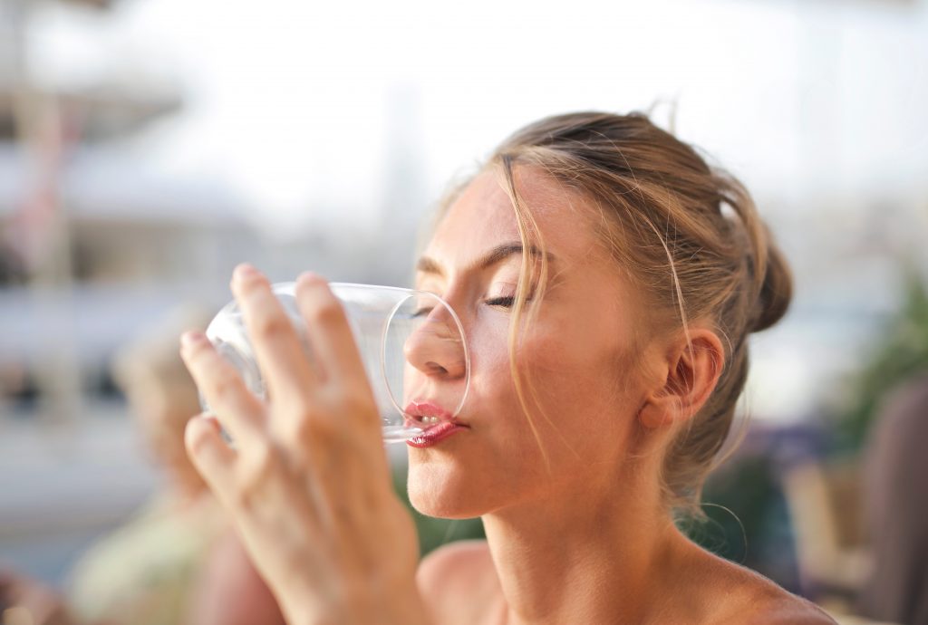 A woman drinking a glass of water, illustrating that excessive water intake can lead to overhydration.