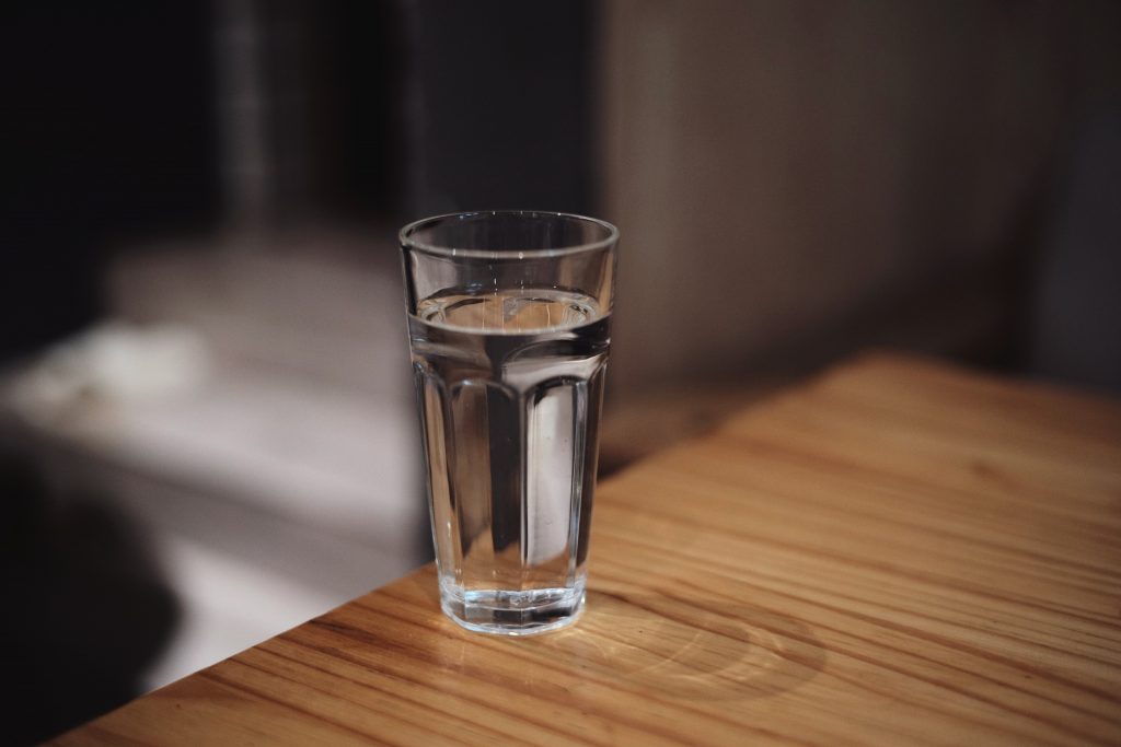 A clear glass of water placed on a wooden table, emphasizing the importance of staying hydrated for overall health.