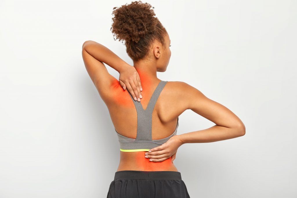 A young woman holding her back, visibly experiencing back pain.