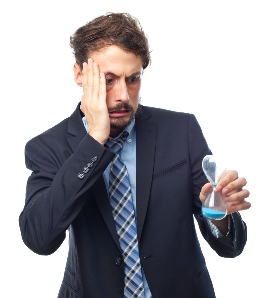 A man dressed in formal attire looking at an hourglass, appearing stressed.