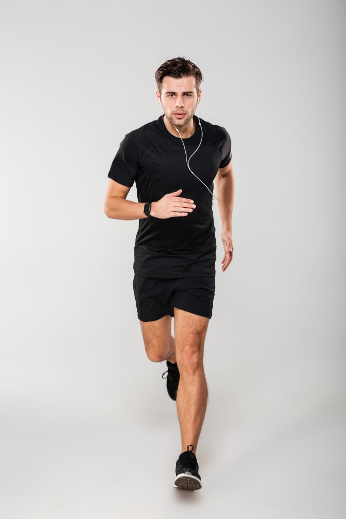 A man wearing earphones jogging with a focused expression.