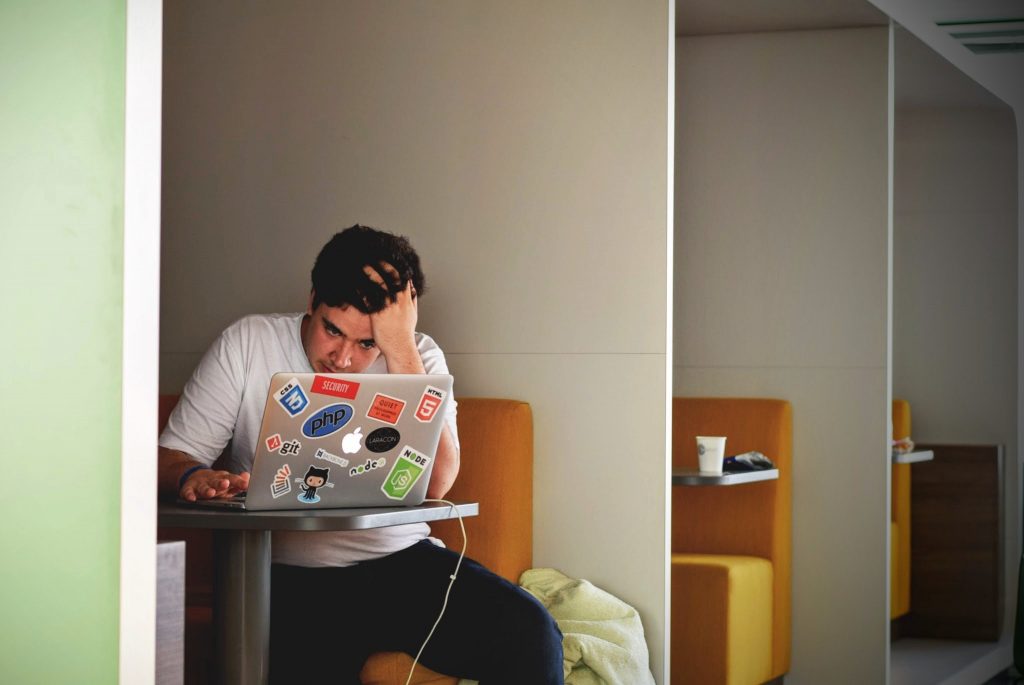 Stressed man sitting at a table with a laptop covered in programming stickers, facing complications from alcohol-related liver disease.