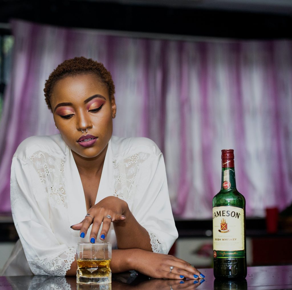 A woman with short hair in a white lace top, sitting with alcohol, highlighting how alcohol affects women’s liver.