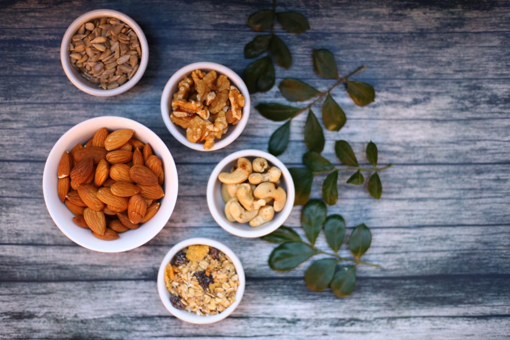 Almonds, walnuts, cashews, and granola in white bowls on a wooden table, highlighting nuts as a safe option for gout.