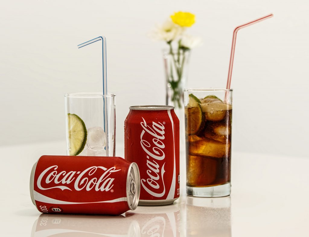 Coca-Cola cans and iced glasses near a flower vase, highlighting how sugary drinks add calories without reducing food intake.