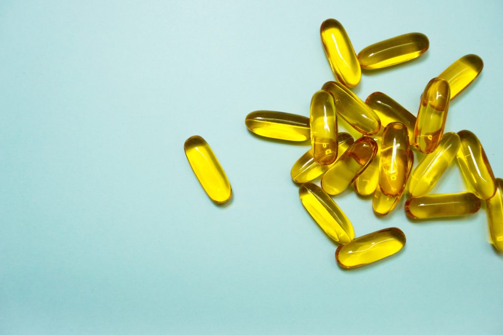 Cod liver oil capsules scattered on a blue background, highlighting their role in supporting lower blood pressure.