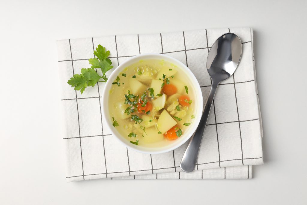 A bowl of vegetable soup with parsley on a checked napkin, helping fill you up without high-calorie foods.