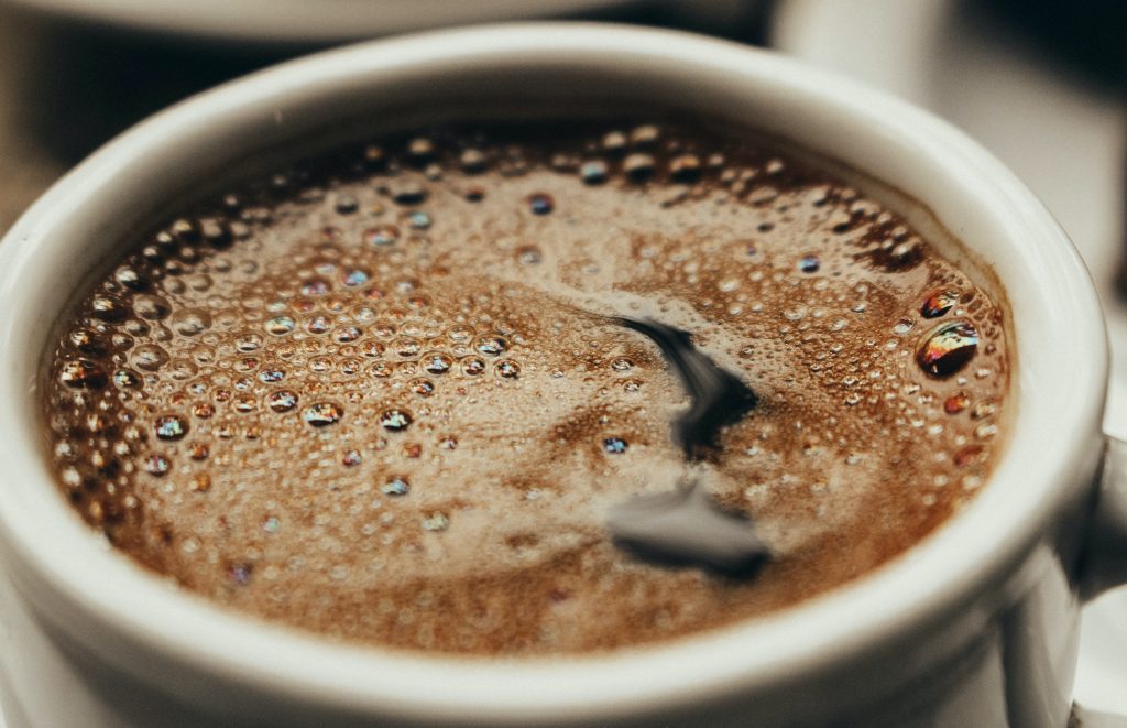 A close-up of a white cup filled with coffee, showing bubbles on the surface, linked to a possible reduced risk of gout.