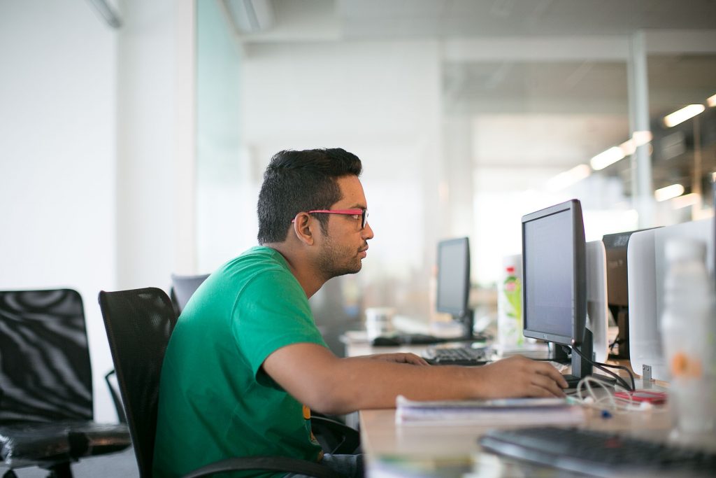 Man in a green shirt working on a computer in an office, illustrating how prolonged sitting can lead to overeating.