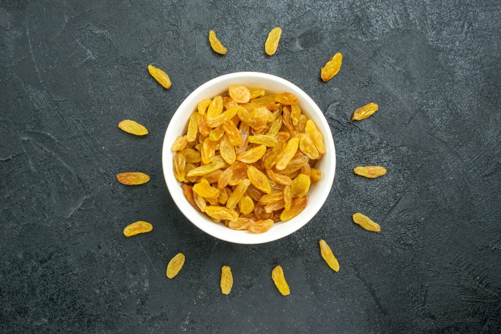 Bowl of golden raisins with scattered raisins, a convenient way to increase your calorie intake.