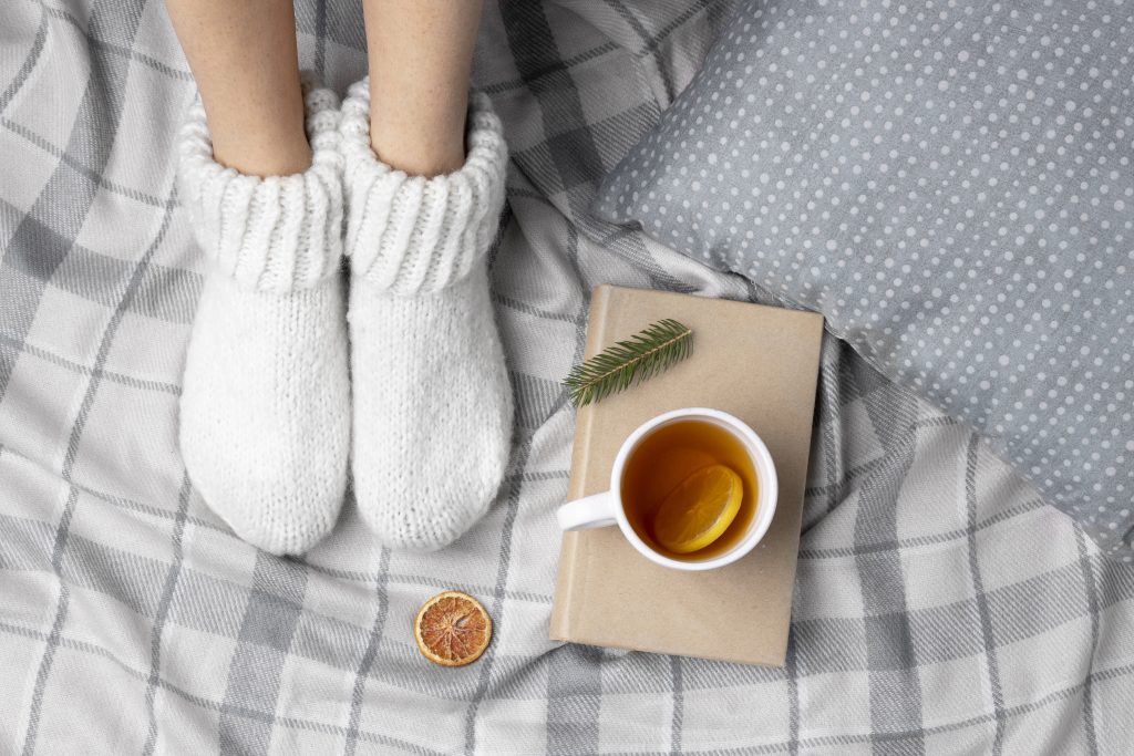 A person in white socks with a cup of tea, highlighting how B12 deficiency causes cold hands and feet from anemia.