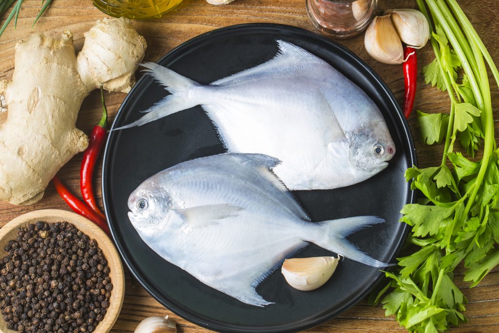 Raw fish high in omega-3 on a sleek black plate, accented with red chili, garlic, ginger, parsley, and peppercorns.