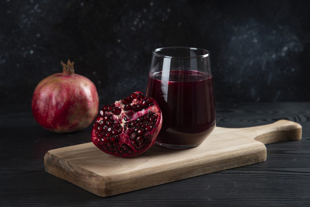 A glass of pomegranate juice with a whole and halved pomegranate, illustrating its role in preventing illness and boosting immunity.