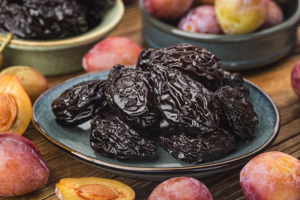 Dried plums on a plate with fresh plums, known for their ability to alleviate constipation.