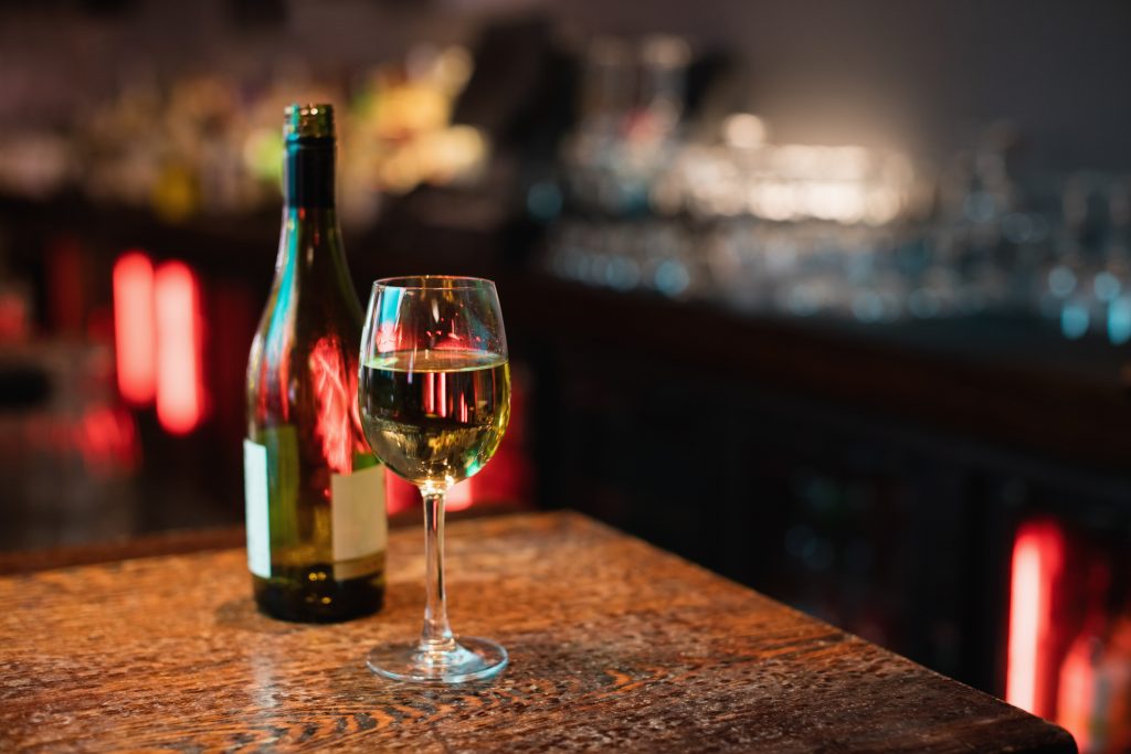 A glass and bottle of alcohol on a table at night, highlighting how heavy drinking is associated with weight gain.
