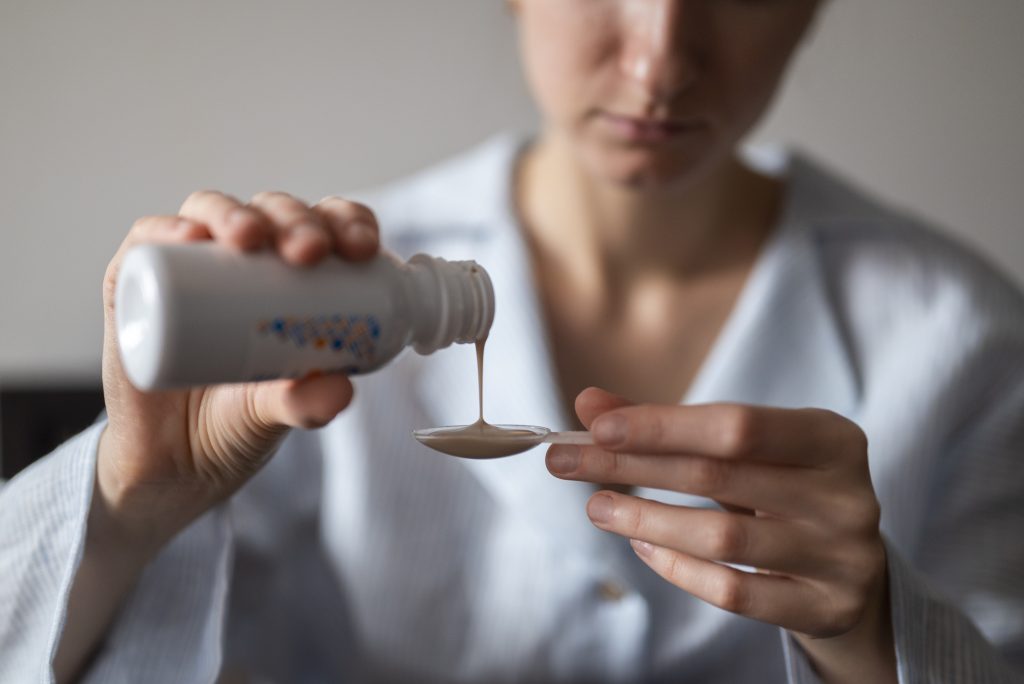Person pouring liquid from a bottle into a spoon, highlighting how some medications can increase the risk of kidney disease.