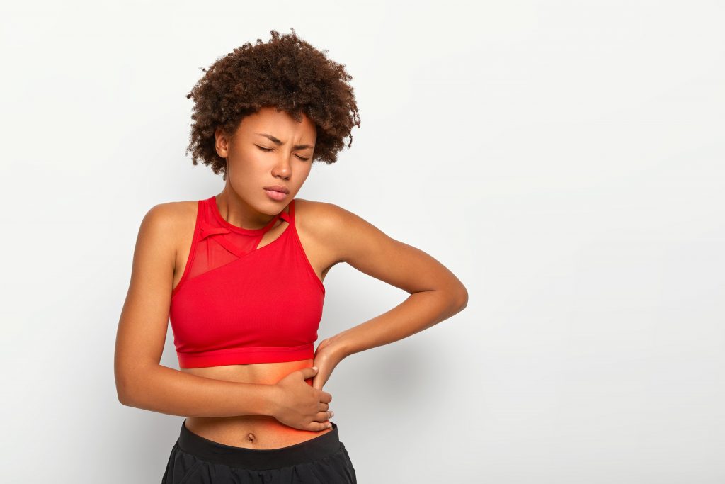 Woman in red sportswear holding her stomach, expressing discomfort, a warning of possible kidney issues.