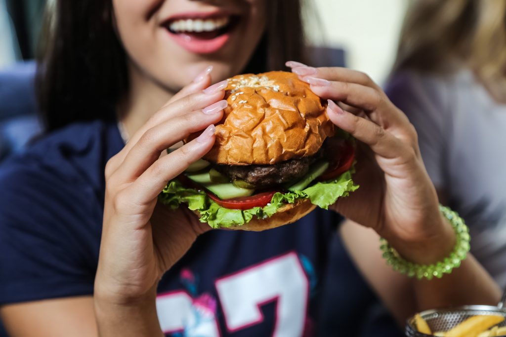 A happy woman holding a burger, highlighting how binge eating can lead to consuming more food than the body requires.