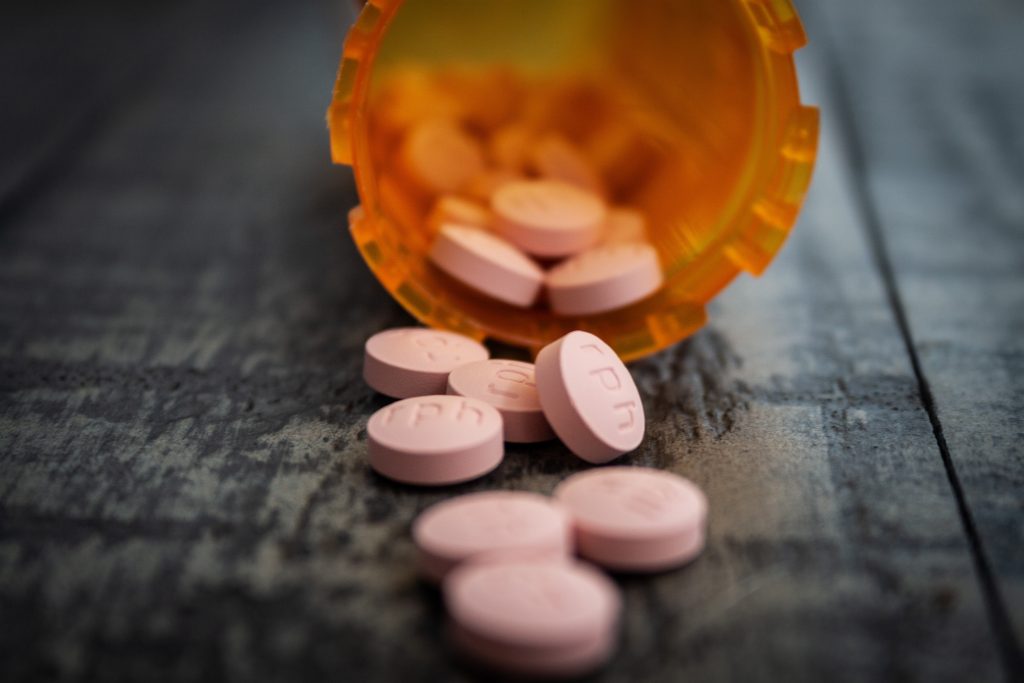 Pink pills scattered from an orange bottle on a dark surface, symbolizing medication for managing hypertension.
