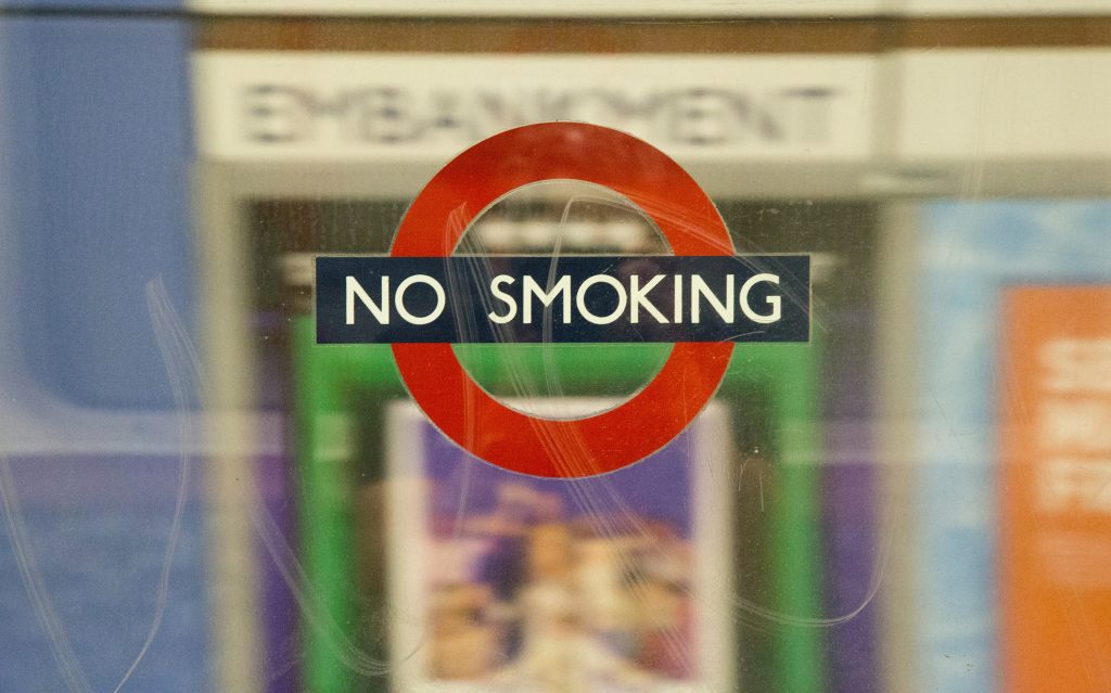 "No Smoking" sign with a red circle and line through a cigarette, attached to a glass window.