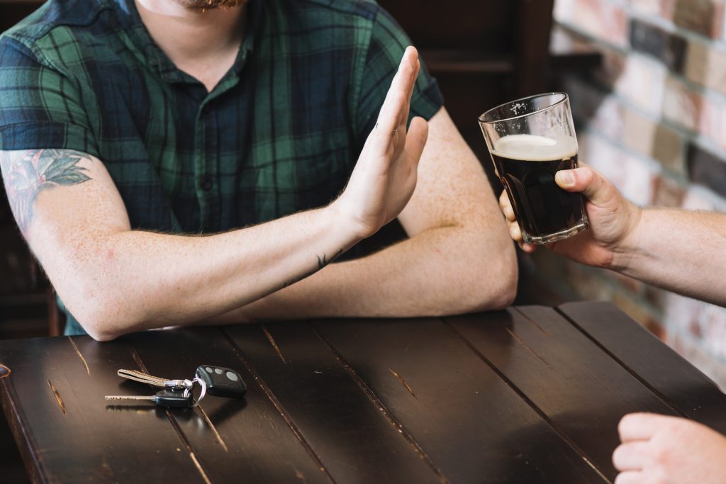 A person with a tattooed arm refusing alcohol, symbolizing the importance of lifestyle changes in treating ARLD.