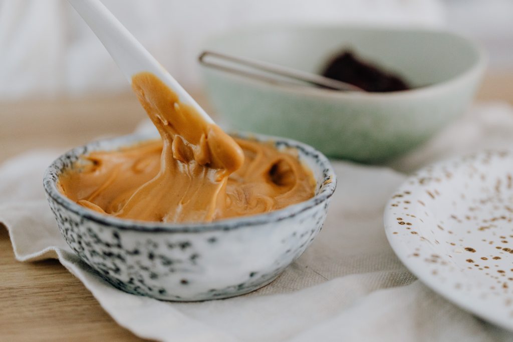 A bowl of creamy peanut butter with a spoon, packed with monounsaturated fats and plant-based protein for a flat belly.