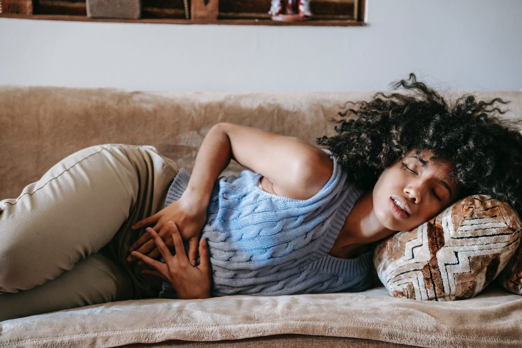 A woman lying on a couch with her hand on her stomach, reflecting the intense impact of period cramps on daily life.