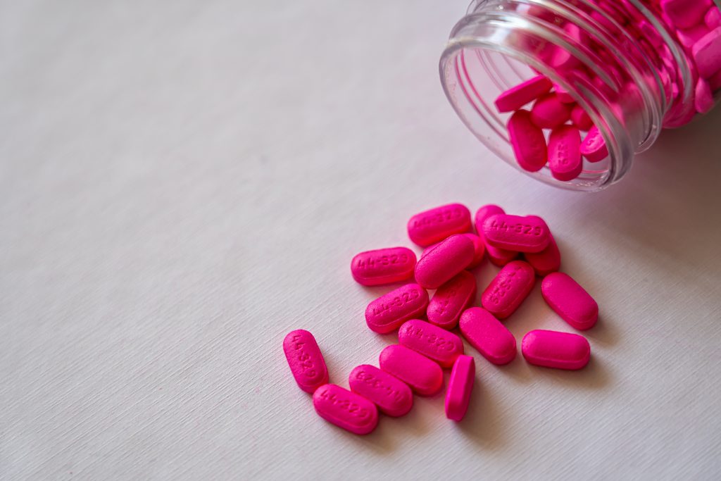 A bottle of pink pills lying flat with some spilled, illustrating how OTC pain relievers ease period cramps effectively.