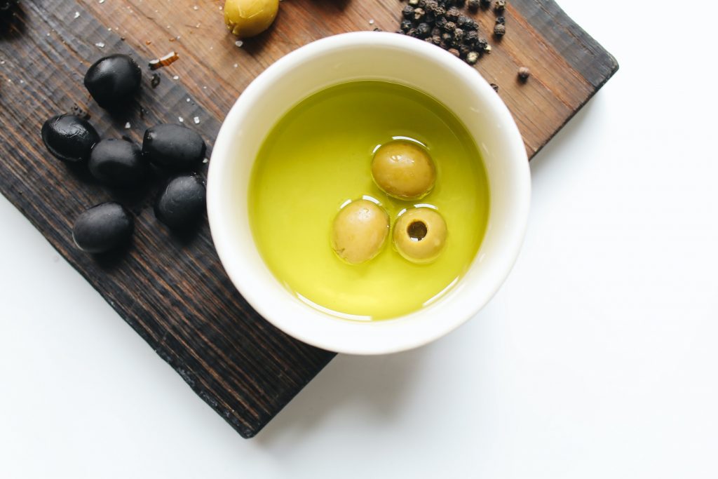 A bowl of green olive oil with olives, and peppercorns on a wooden board, highlighting fat-fighting foods.