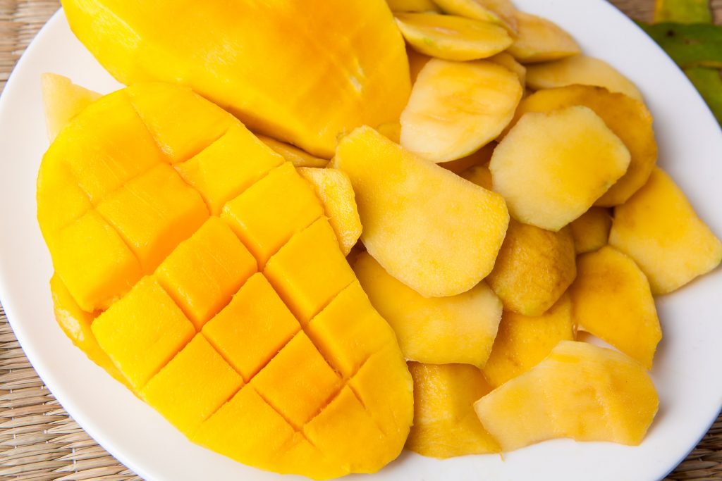 Cubed bright yellow mango slices on a white plate, showcasing a delicious, nutrient-rich fruit.