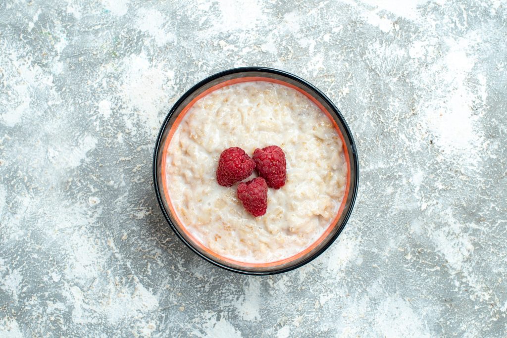 A bowl of oatmeal topped with three raspberries, showcasing the fiber-rich properties of whole grains for lasting fullness.