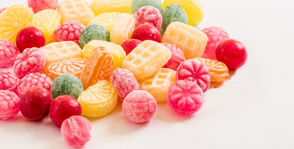 A display of fruit-colored candies and jelly, emphasizing the impact of sugars and refined carbs on weight gain and obesity.
