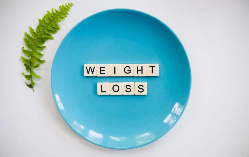 Blue plate with Scrabble tiles spelling "WEIGHT LOSS" and a green garnish, symbolizing lifestyle tips for weight reduction.
