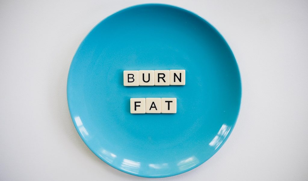 A blue plate with "Burn Fat" spelled out in Scrabble tiles, symbolizing the impact of boosting metabolism on fat loss.