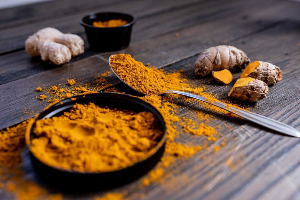 Turmeric powder in a bowl with roots and scattered powder, highlighting curcumin's anti-inflammatory and antibacterial properties.