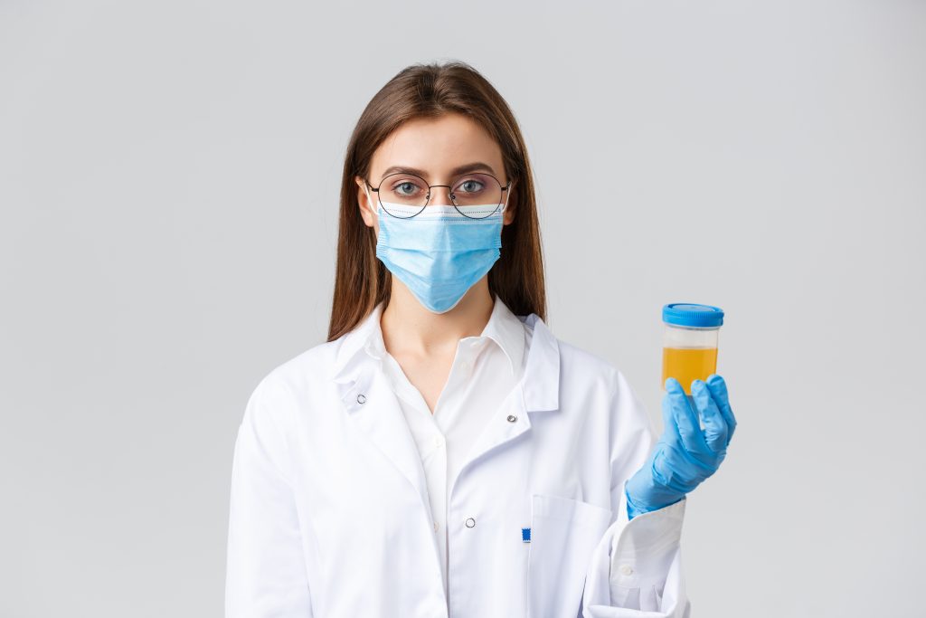 Health professional with glasses, mask, and gloves holding a urine sample, checking for signs of blood leakage due to faulty kidneys.