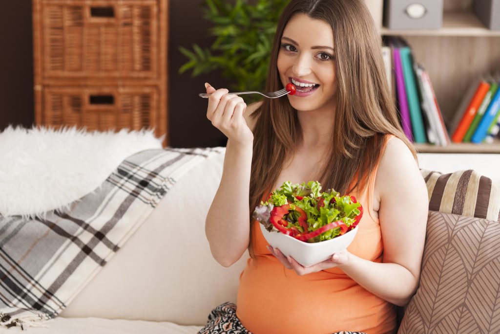 A pregnant woman enjoying salad on the couch, emphasizing the importance of B12 supplements during pregnancy and breastfeeding.
