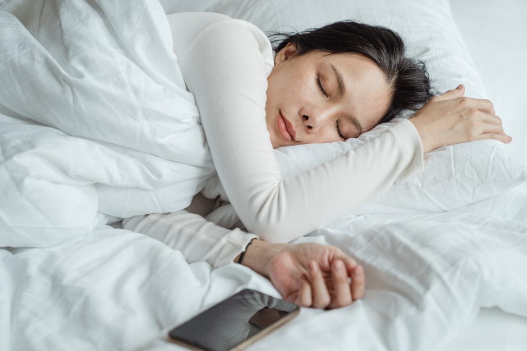 A woman sleeping peacefully with her smartphone nearby, highlighting the role of smart sleep in relieving period pain.