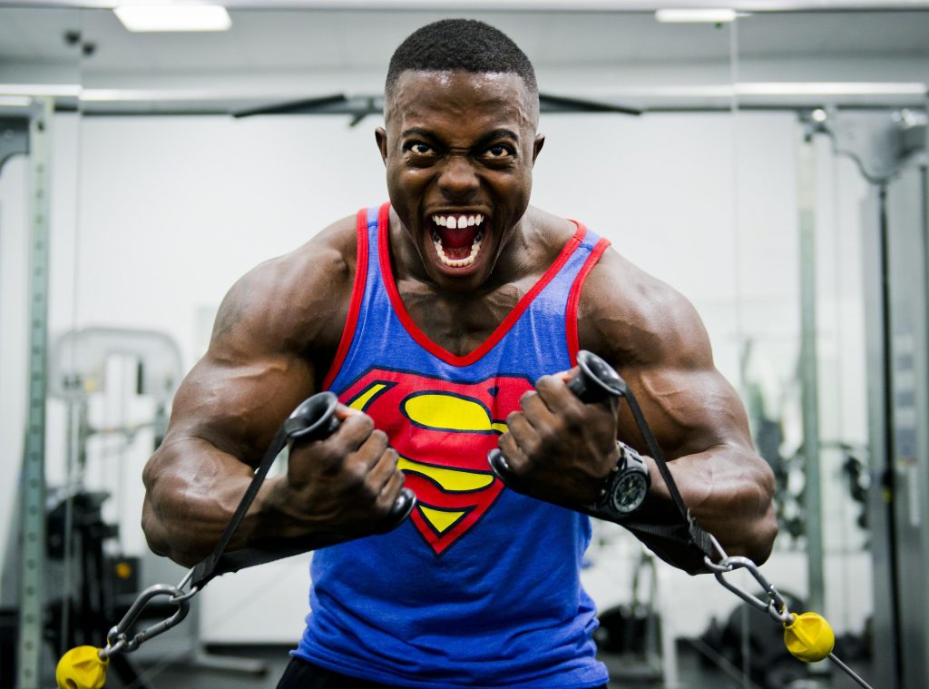 Muscular man training with resistance bands, pushing too hard in the gym, risking rapid muscle tissue breakdown.