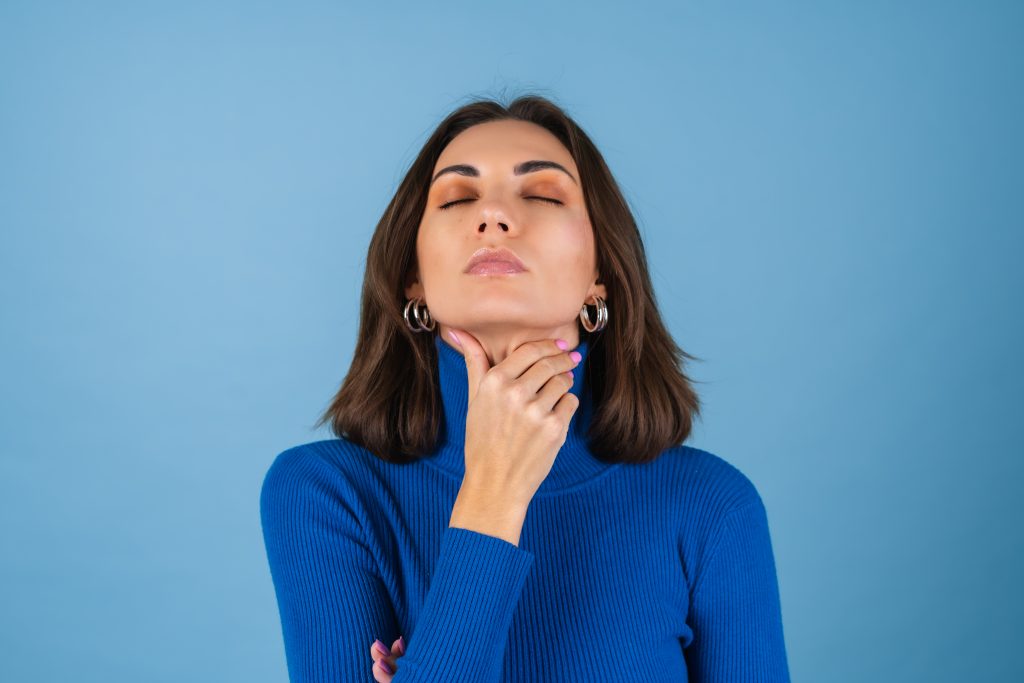 Woman in a blue high-neck sweater, gently touching her neck, symbolizing how underlying health conditions can hinder weight loss.